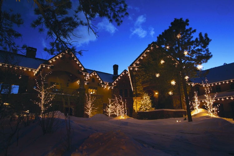 Home decorated with warm holiday string lights glowing against a snowy dusk sky