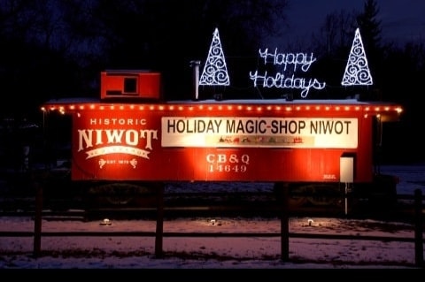 Historic Niwot caboose strung with warm holiday lights glowing against a snowy night